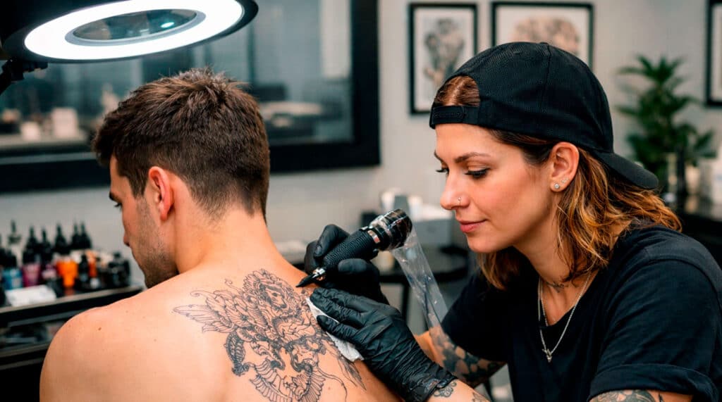 Tatuadora profesional realizando un tatuaje corporal con técnica aséptica y guantes