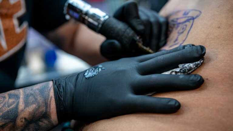 Tatuador con guantes negros trabajando con la máquina sobre el brazo de un cliente