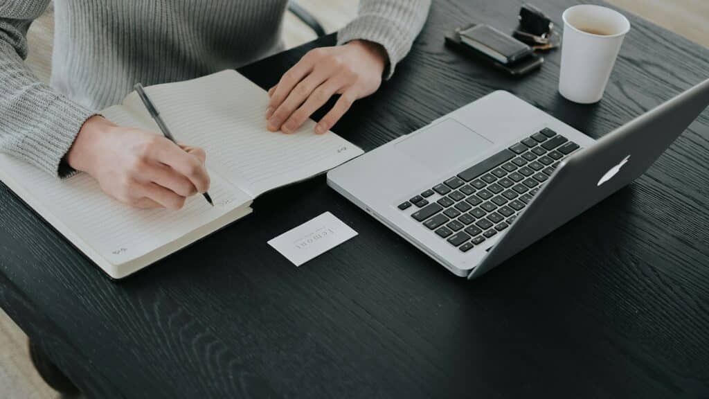 Persona tomando apuntes en un cuaderno junto a un portátil