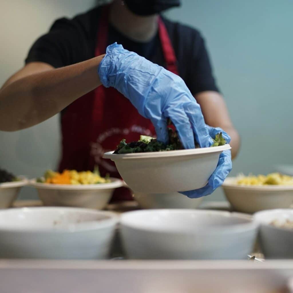 Persona con delantal y guantes azules sirviendo comida en un cuenco
