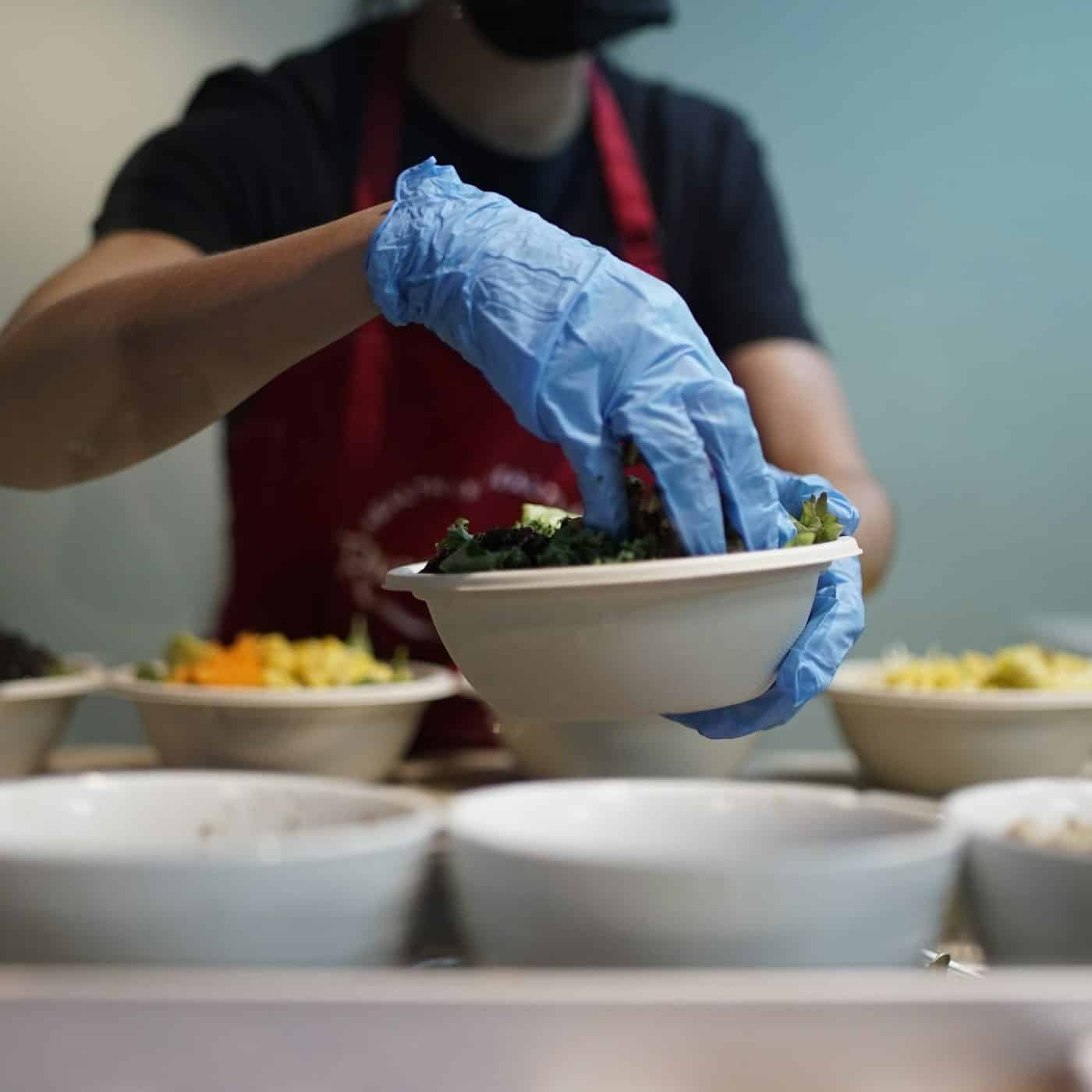 Persona con delantal y guantes azules sirviendo comida en un cuenco