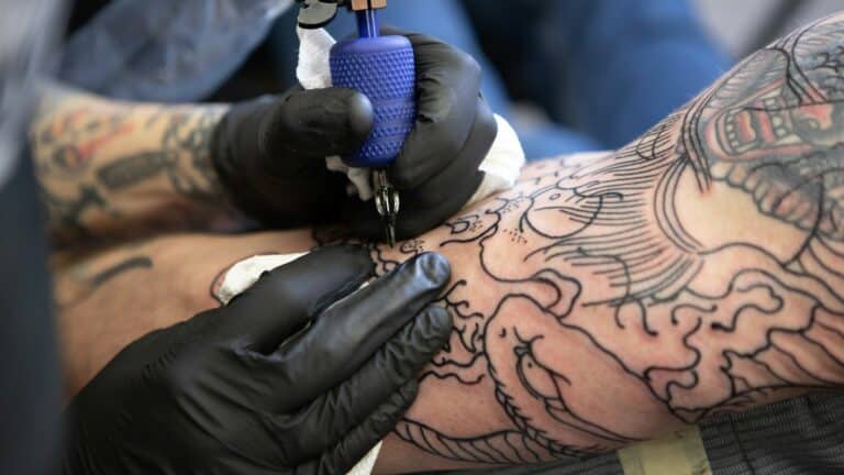 Tatuador con guantes de nitrilo negros tatuando el brazo de un cliente