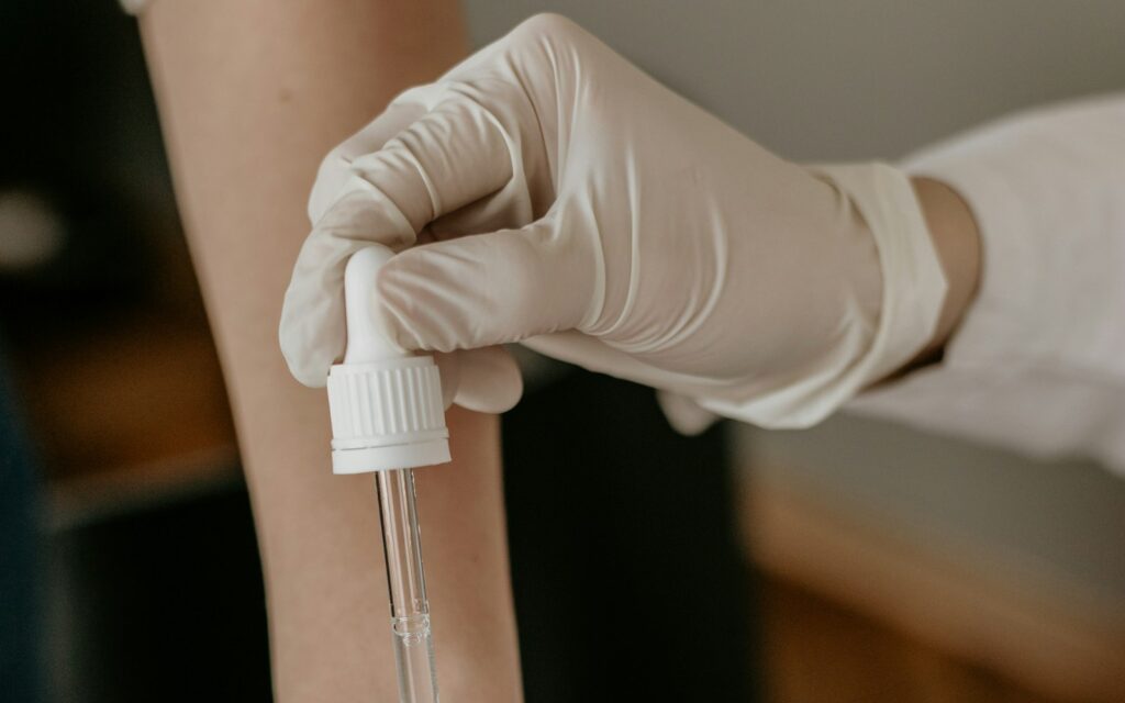 Mano con guante aplicando un sérum con cuentagotas sobre la piel del antebrazo