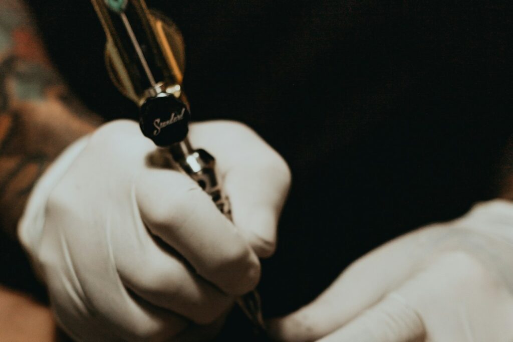 Manos de tatuador con guantes desechables sujetando la máquina de tatuar