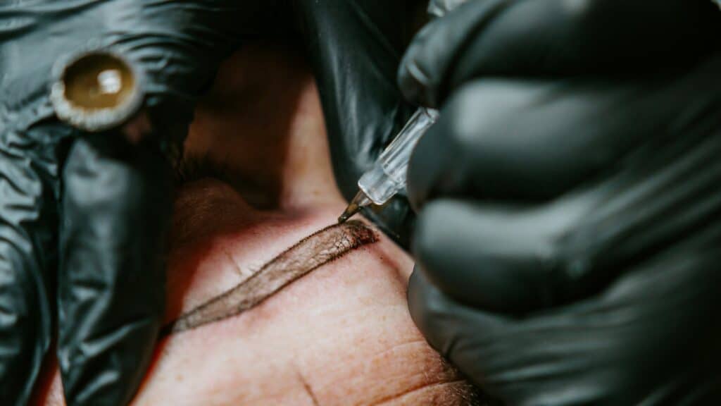 Profesional con guantes realizando un microblading de cejas